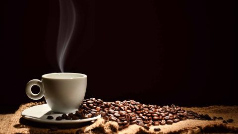 Cup of coffee with smoke and coffee beans on black background